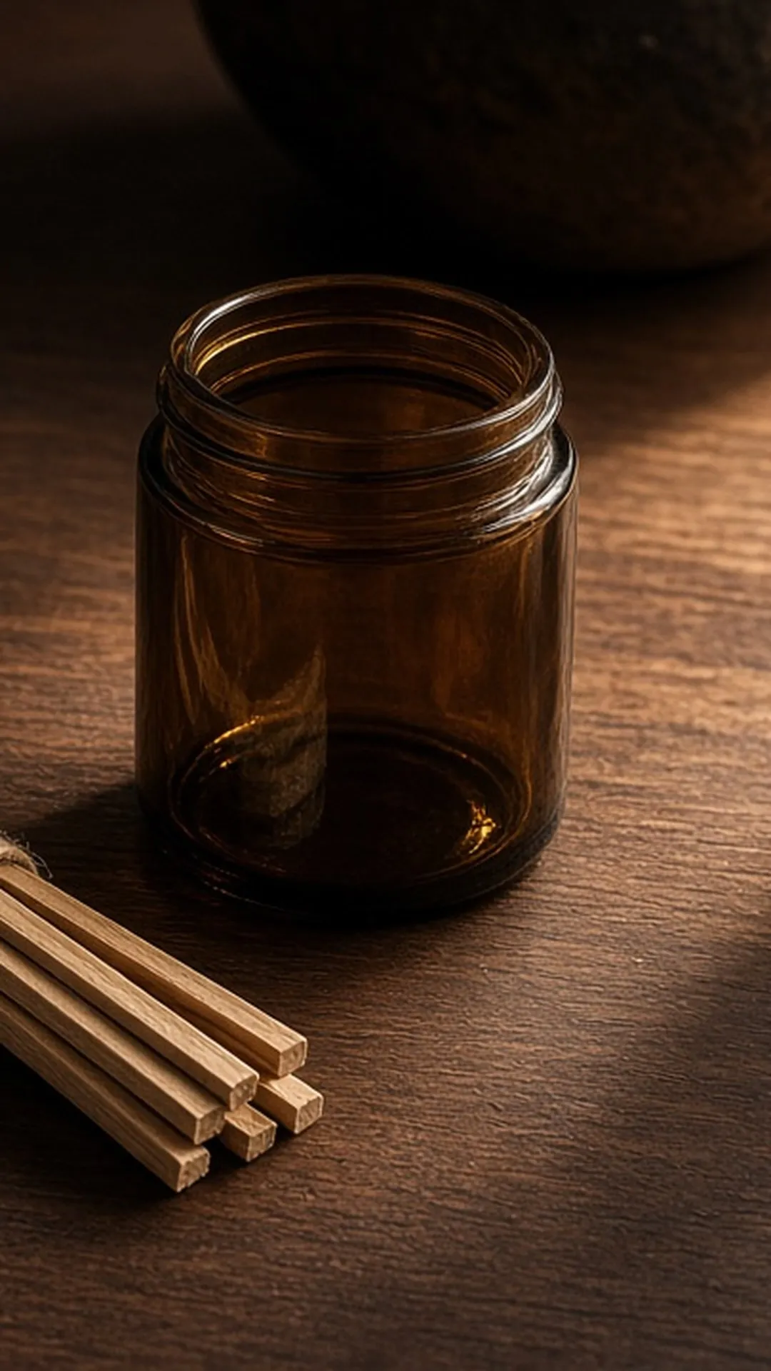 A bundle of thin wooden wicks tied with twine beside an empty amber jar on a walnut table